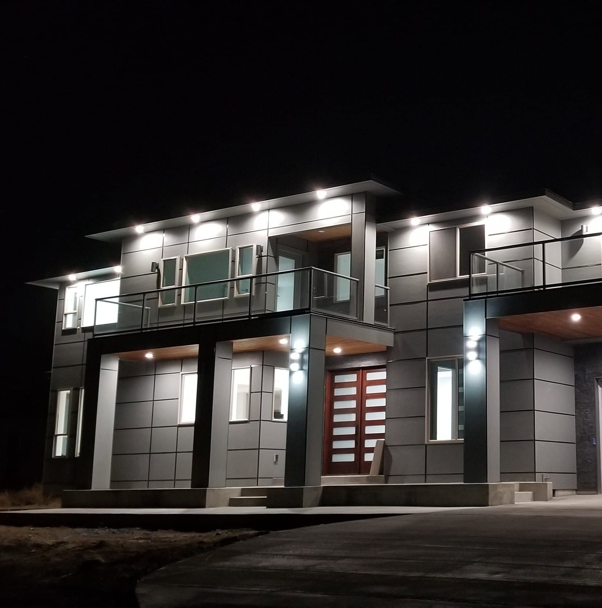 Two-story modern house at night with soffit downlights across the roofline and entry