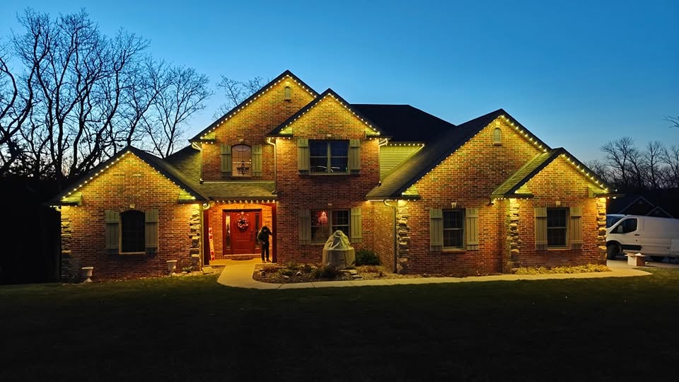 The same brick house lit in warm white along every gable