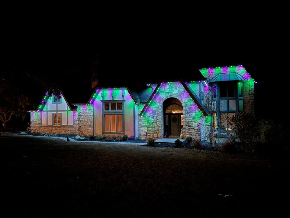 Stone and stucco house at night lit in purple and green along the rooflines