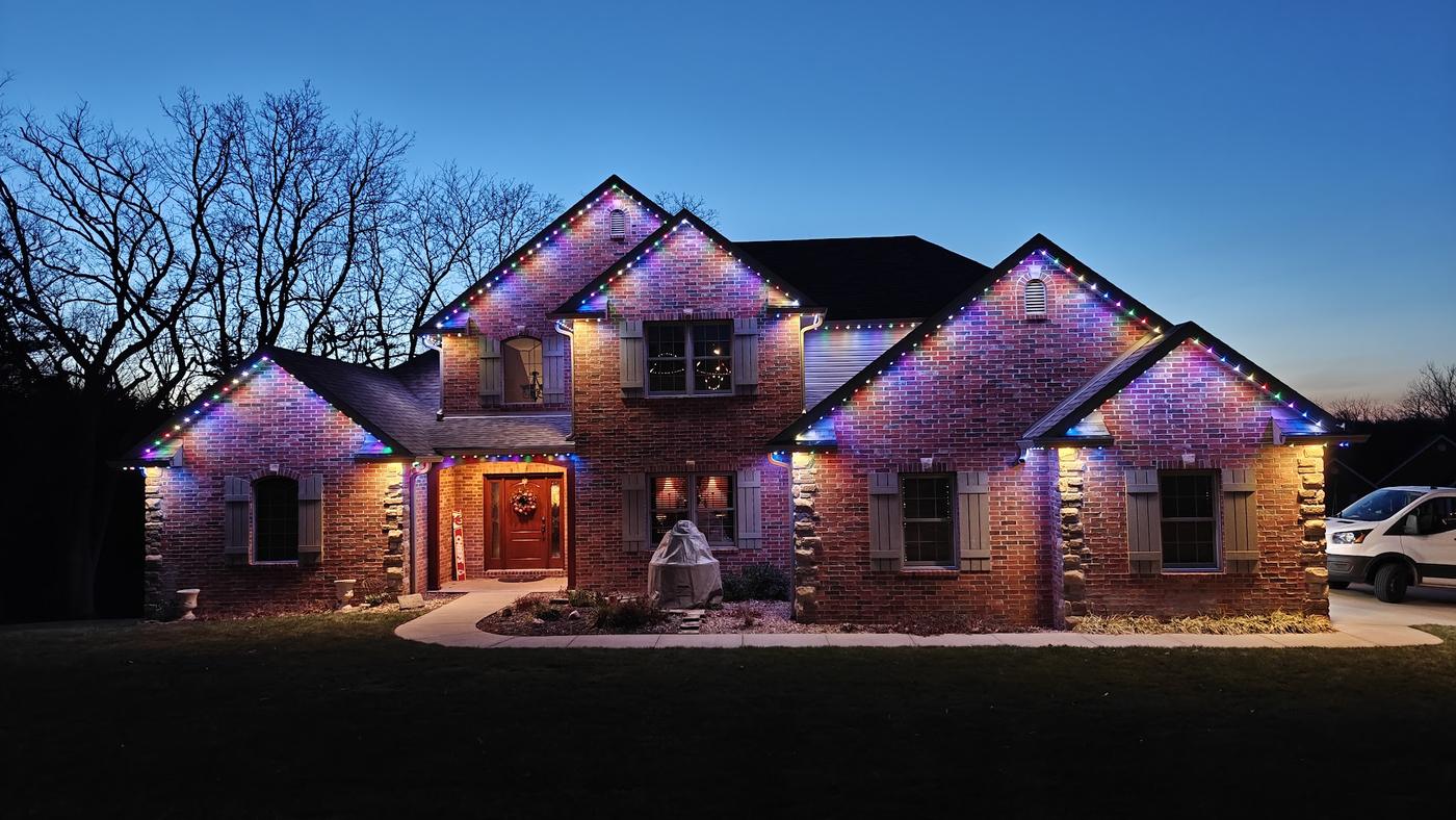 Brick two-story house at dusk with multicolor roofline lighting and a work van in the driveway