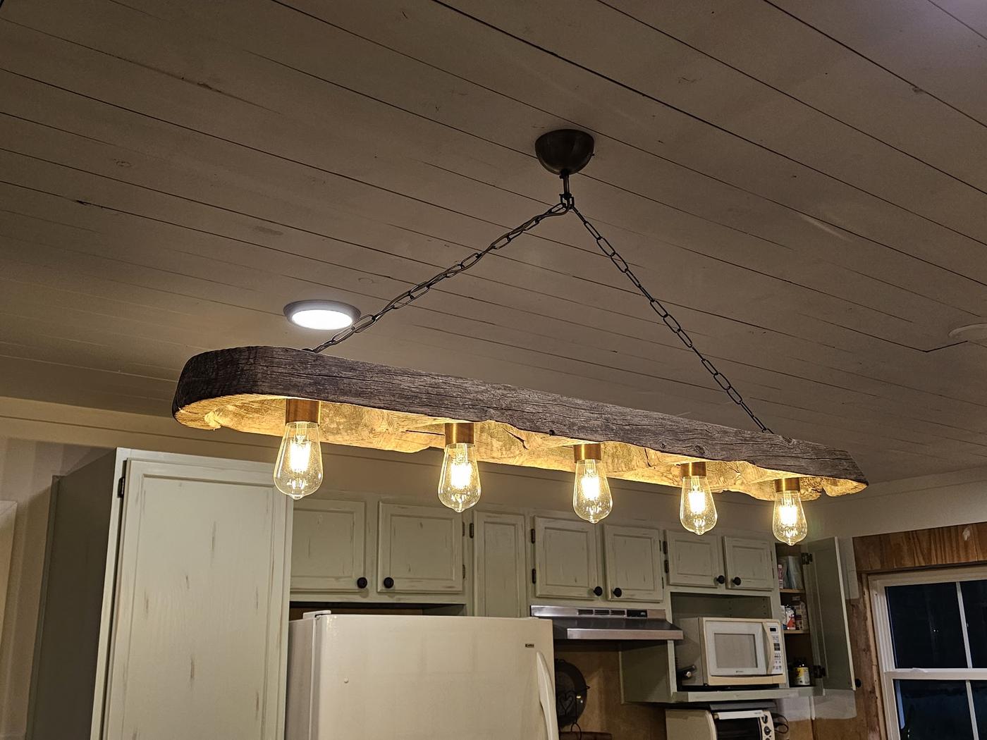 Five exposed bulbs mounted along a reclaimed beam hung over a kitchen