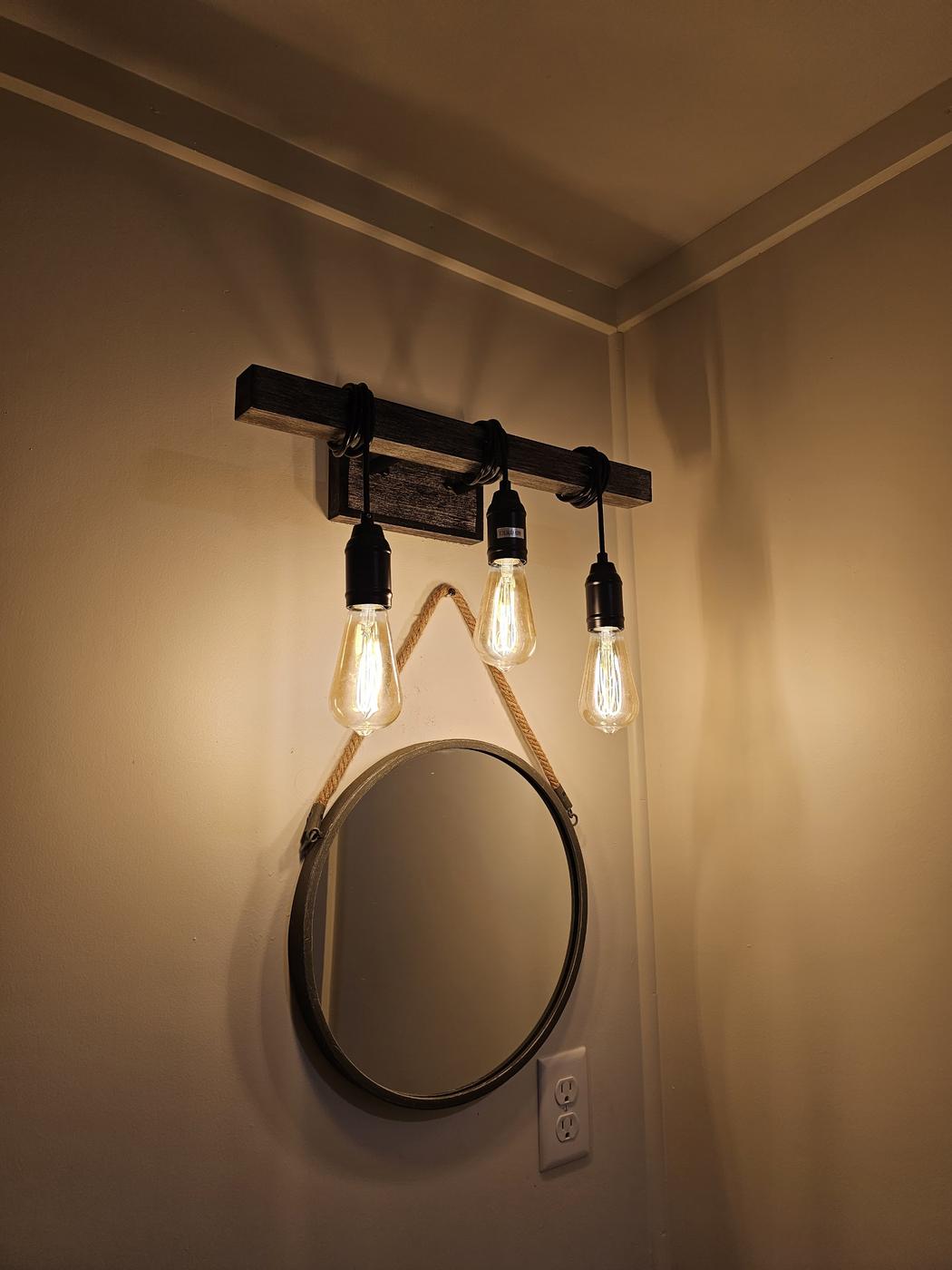 Three pendant bulbs hung above a round mirror in a bathroom
